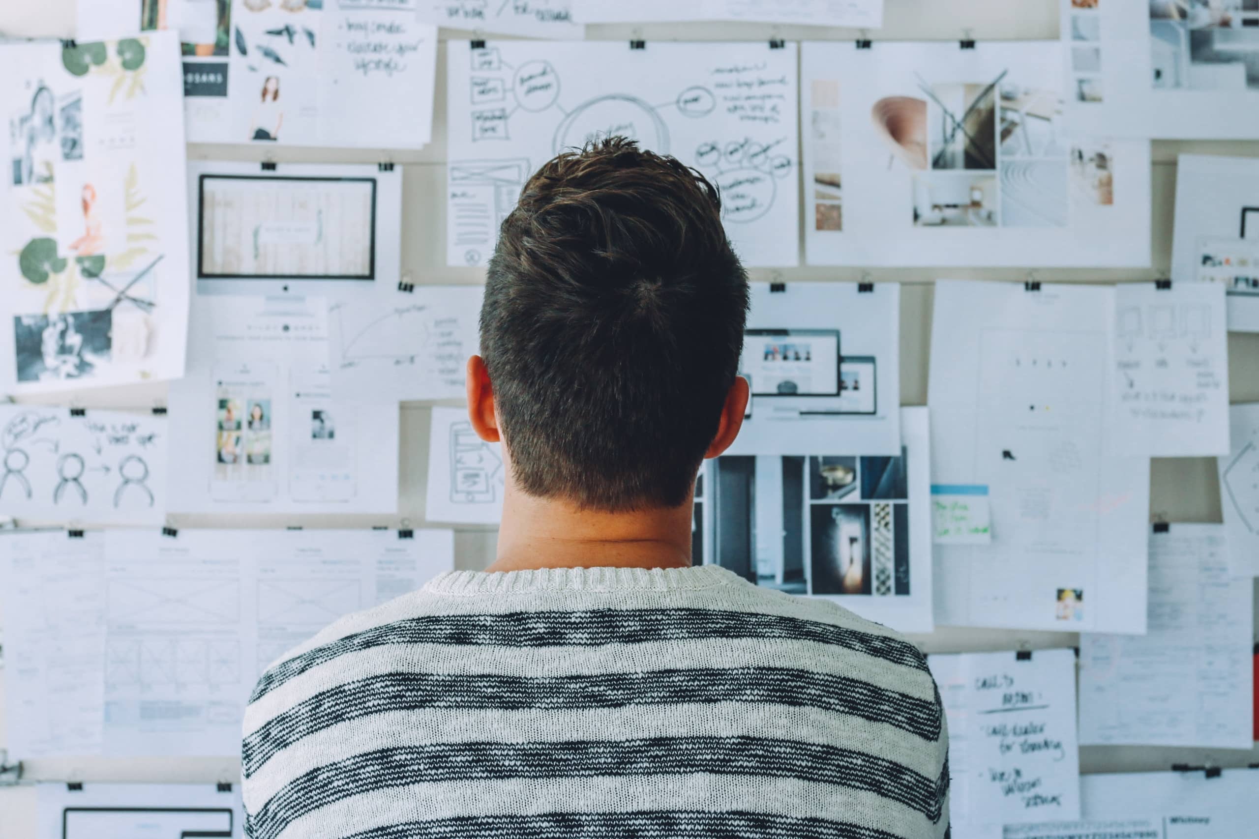 man-wearing-black-and-white-stripe-shirt-looking-at-white-printer-papers-on-the-wall